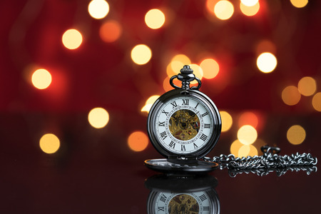 Vintage pocket watch symbol with party decoration light bokeh in the red background before midnight,...