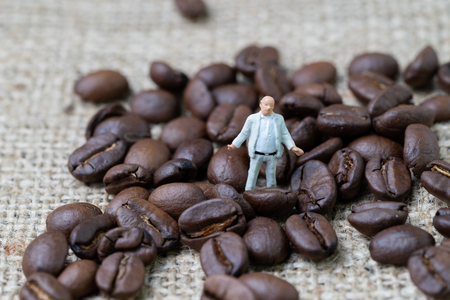 Coffee business expert or professional concept, miniature rich man business owner figurine standing with roasted coffee beans on gunny bag background, selecting best aroma quality.の写真素材