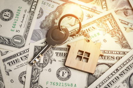 House, mortgage loan or real estate business concept, key with wooden house key chain on pile of US...