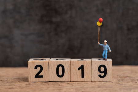 Year 2019 new year changing concept, miniature people happy man holding balloons on cube wooden...
