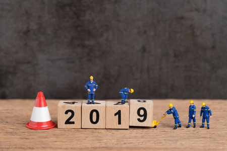Year 2019 new year changing or just finished concept, miniature people workers building cube wooden block number 2019 with under construction sign and traffic cone, dark background with copy space.の写真素材