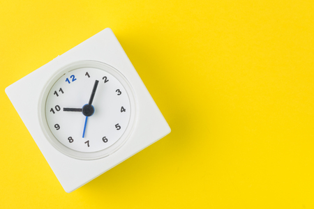 Time, deadline or reminder and schedule concept, minimal modern square alarm clock with white face on yellow background in flat lay or top view, studio shot with copy space.の写真素材