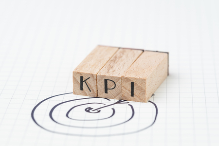 Key Performance Indicator, KPI concept, small wooden stamp combine the acronym KPI with hand draw arrow and target on white grid paper. Metric or measurement to achieve or success in business.の写真素材