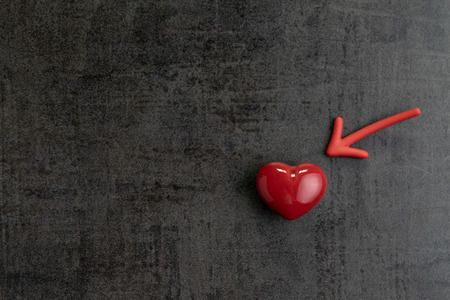 Red magnet arrow pointing to shiny ceramic red heart shape on cement chalkboard wall, minimal concept for Happy Valentine's day.の写真素材