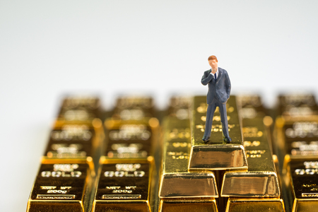 Success wealth management concept, miniature figure businessman standing on stack of shiny gold bar bullions ingot with copy space white background.の写真素材