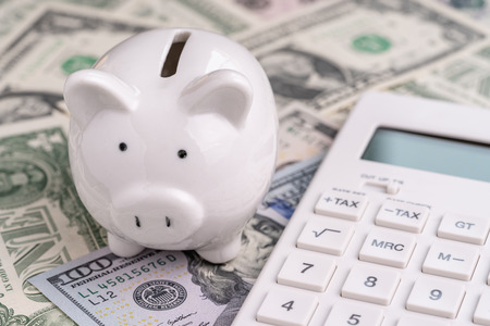 Accounting, finanacial investment or budget concept, cute white piggy bank or coin bank and calculator on pile of US America Dollar banknotes money.の写真素材