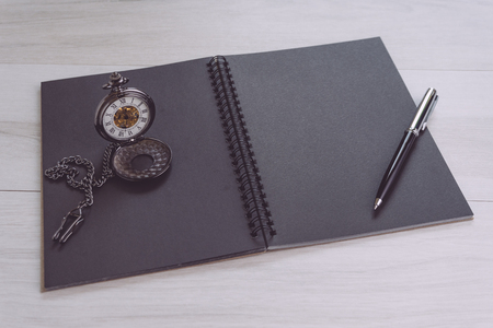 Blank empty black page note book opening with pen and vintage pocket watch on gray wooden table using as time, journal thinking, writing and creativity.の写真素材