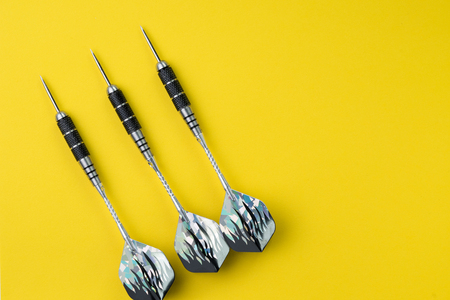 3 perfect black darts flat lay on solid yellow background with copy space using as target and goals...