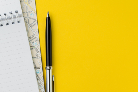 Flat lay or top view of black pen, notepad and map on vivid yellow background table with blank copy space, tourist, vacation or travel destination plan concept.の写真素材