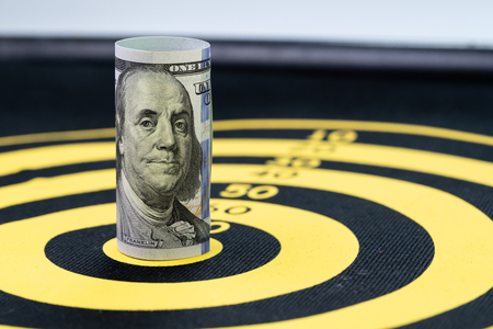 Financial goal or target concept, US Dollar banknote roll targeted at the center of yellow dartboard.の写真素材