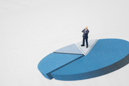 Miniature success and confidence businessman in suit standing on performance pie chart with black calculator using as work report, management profit and loss or company achievement and analysis.の写真素材