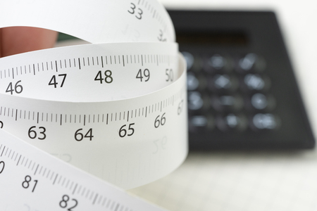 White measurement tape roll with number of centimeter and inch with calculator on white background with copy space using as health, diet or measuring tool concept.の写真素材