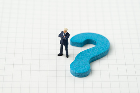 Start with why, asking quesion and answer concept, miniature business man standing with blue wooden quesion mark symbol on white grid line note book paper.の写真素材