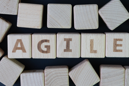 Agile software development concept, cube wooden block with alphabet building the word Agile at the center on dark blackboard background, requirements and solutions evolve through collaborative effort.の写真素材