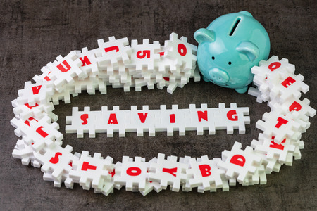 Saving idea for financial target, abundance white puzzle jigsaw with alphabets combine word SAVING and other letter pieces around with blue piggy bank and dark black chalkboard cement wall.の写真素材