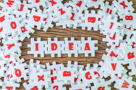 Business idea, creativity or inspiration in work and problem solving, abundance white puzzle jigsaw with alphabets combine word IDEA surround by other alphabets on wooden table background.の写真素材