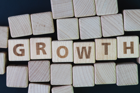 Business growth, company expand to get more revenue concept, cube wooden block with alphabet building the word Growth at the center on dark blackboard background, new opportunity in career path.の写真素材