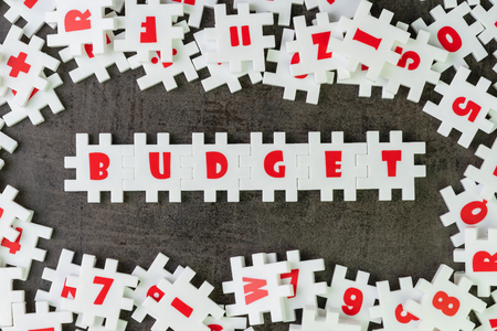 Budget idea, abundance white puzzle jigsaw with alphabets combine word BUDGET and other letter pieces surrround and dark black chalkboard cement wall.の写真素材