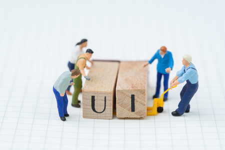 Building UI, User Interface concept, miniature people figure, workers, engineers building or moving wooden stamp block to arrange the abbreviation UI on grid line idea notebook.