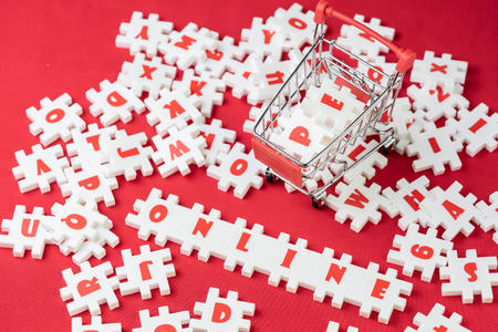 Online shopping concept, white puzzle jigsaws with alphabets building the word Online with shopping cart or trolley on red fabric background.の写真素材