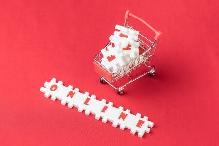 Online shopping concept, white puzzle jigsaws with alphabets building the word Online with shopping cart or trolley on red fabric background with copy space.の写真素材