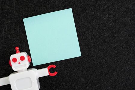 Chatbot, AI Artificial Intelligence concept, blue blank sticky note with vintage robot on dark black...
