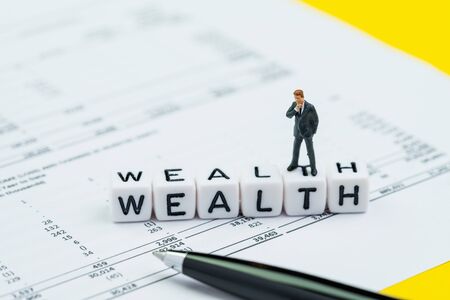 Wealth management, success investment or financial independent concept, miniature businessman standing and thinking on cube block building the word Wealth on profit and loss report with numbers.の写真素材