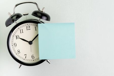 Reminder, time, deadline, stop procrastination or meeting schedule concept, alarm clock with blank sticky note on top for text and message on white background with copy space.の写真素材