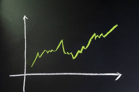 Stock and investment growth, dark black blackboard with chalk drawing green line as stock return growth graph with copy space.の写真素材