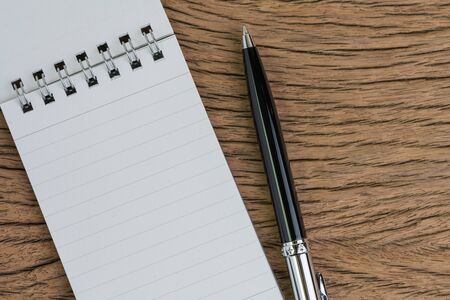 Small paper notepad with blank page, pen on wooden table using as meeting note, writing message or...