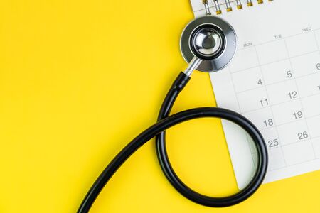 Medical and health care calendar, reminder, schedule or appointment concept, doctor's stethoscope on white clean calendar with date on solid yellow background with copy space.の写真素材