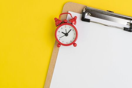 Clipboard with empty white paper with read alarm clock on solid yellow background with copy space for writing message using as stop procrastination, memo, reminder or record idea.の写真素材