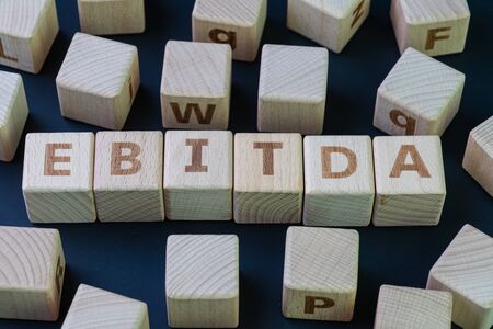 EBITDA, Investment term Earnings before interest, taxes, depreciation, and amortization concept, cube wooden block with alphabet combine the word EBITDA on black chalkboard background.の写真素材