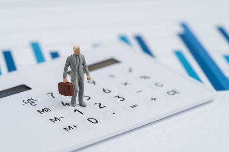 Business performance, KPI, key performance indicator or company revenue or profit on management, miniature people businessman leader in suit carrying suitcase on calcultaor, bar graph report.の写真素材