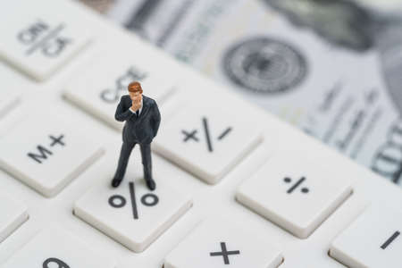 Miniature people business man standing and thinking on calculator percentage button using as FED...