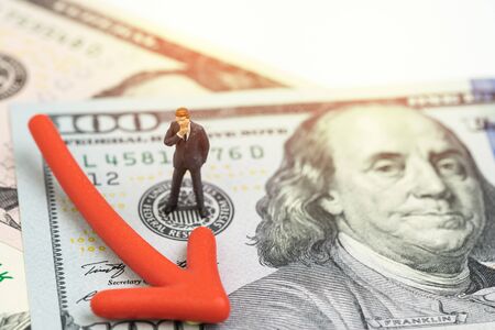 Miniature businessman standing on Federal Reserve, FED emblem on US dollar banknote money with red pointing down arrow using as interest rate cut policy or US economic recession concept.の写真素材