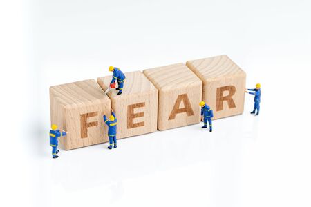 Cube wooden block with alphabets combine the word FEAR with miniature people men help building on...