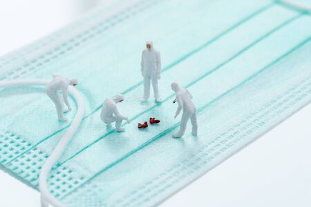 miniature people doctor team wearing protective suit and mask diagnose some Virus pathogen on hygienic mask using as  protection, research for vaccine or patient treatment concept.の写真素材