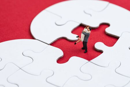 Miniature people love couple man and woman holding each other at the missing piece of jigsaw heart shape on red background using as Valentines, wedding or love romantic relationship.の写真素材