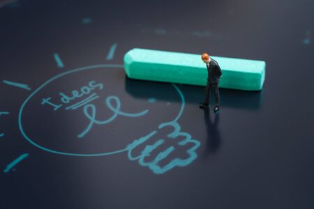 Idea, brainstrom or business solution concept, miniature people businessman in suit standing and thinking on chalkboard with chalk writing light bulb and the word ideas.の写真素材