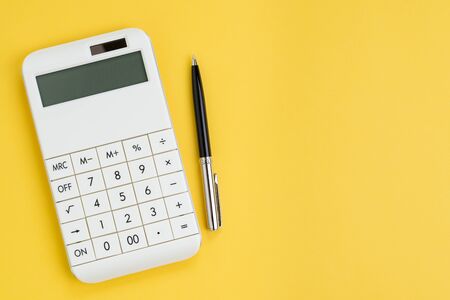 Cost, expense calculation or finance and investment concept, white clean modern calculator with pen on solid yellow background with copy space.の写真素材