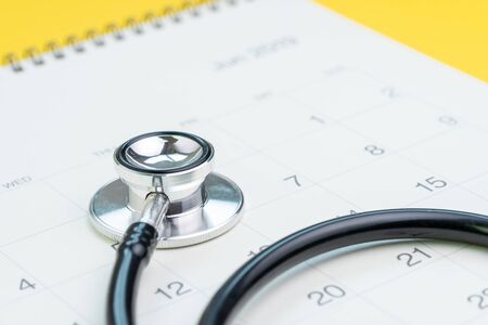 Annual health checkup, medical appointment or examination schedule, doctor stethoscope on white clean calendar on solid yellow background.の写真素材