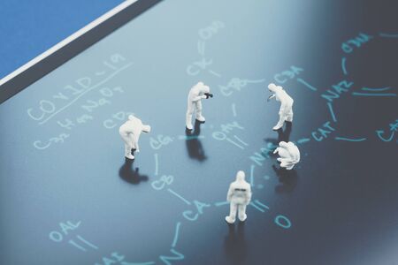 Miniature people doctors with protective suit and mask working on chemical compound on blackboard...