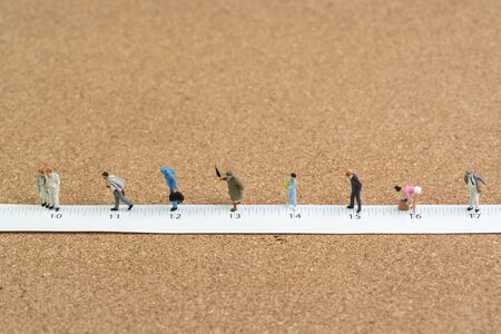 Social distancing, people keep distance in public to protect COVID-19 coronavirus spreading concept, miniature people, men, kids, elderly couple wait in line keep distance away on measuring tape.の写真素材