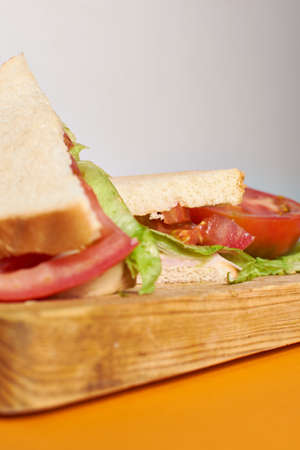 A ham and cheese sandwich with tomato an lettuce in wood board tableの写真素材