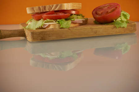 Healthy ham and cheese sandwich with tomato and lettuce in orange backgroundの写真素材