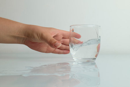 Hand catching glass of water splashing on white background