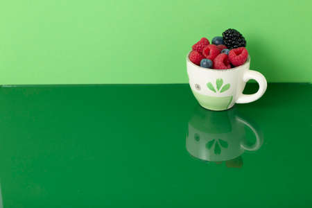 Cup with red fruits on green background with mirror effectの写真素材