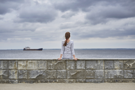 A girl sitting on the embankment of the river with her back to the photogroupの写真素材
