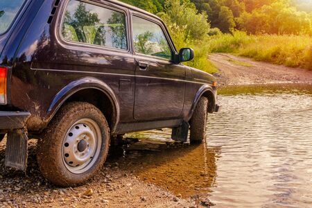 Off-road vehicle at a ford across the river in the glowing light of sunrise. Adventures in nature.の写真素材